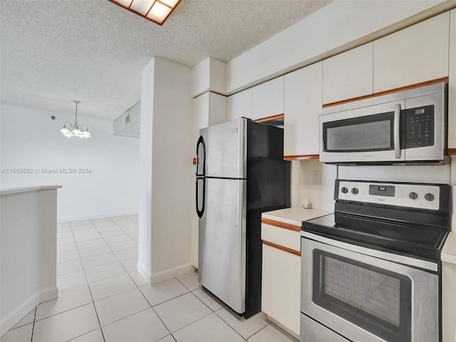 kitchen with appliances with stainless steel finishes, white cabinets, light tile patterned floors, an inviting chandelier, and decorative light fixtures