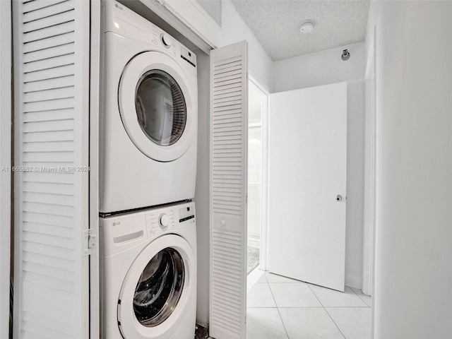 laundry area with light tile patterned floors, a textured ceiling, and stacked washer and dryer