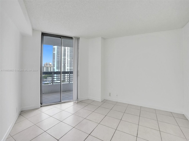 empty room featuring a textured ceiling, floor to ceiling windows, and light tile patterned floors