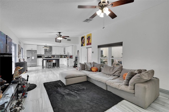 living room with a textured ceiling, ceiling fan, and lofted ceiling