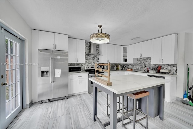 kitchen featuring appliances with stainless steel finishes, light stone counters, wall chimney exhaust hood, white cabinets, and hanging light fixtures