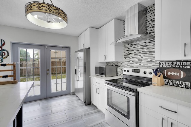 kitchen featuring french doors, wall chimney exhaust hood, stainless steel appliances, pendant lighting, and white cabinets