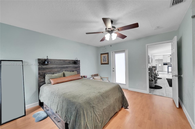 bedroom with ceiling fan, light hardwood / wood-style floors, and a textured ceiling