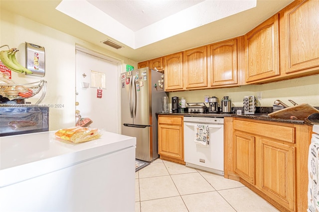 kitchen with dark stone counters, white dishwasher, refrigerator, light tile patterned floors, and stainless steel refrigerator