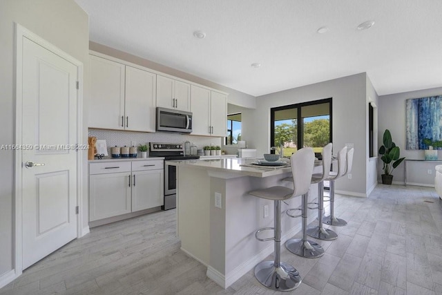 kitchen with a center island, white cabinetry, appliances with stainless steel finishes, a breakfast bar area, and light hardwood / wood-style flooring