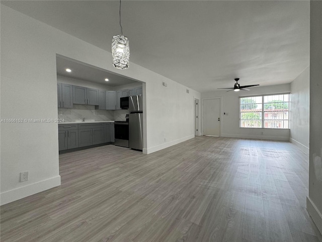 unfurnished living room featuring ceiling fan with notable chandelier and light hardwood / wood-style floors