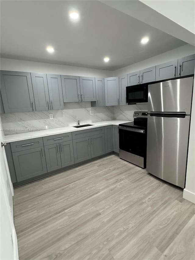 kitchen with stainless steel appliances, light hardwood / wood-style floors, tasteful backsplash, and gray cabinetry