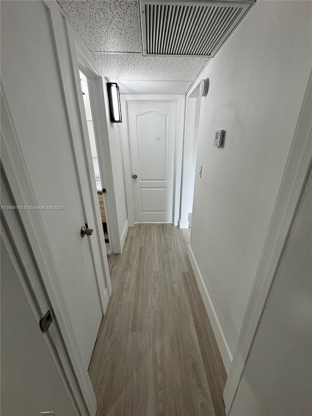 hall with light wood-type flooring and a paneled ceiling