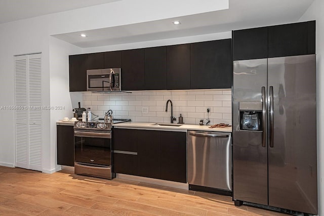 kitchen featuring appliances with stainless steel finishes, sink, decorative backsplash, and light hardwood / wood-style flooring