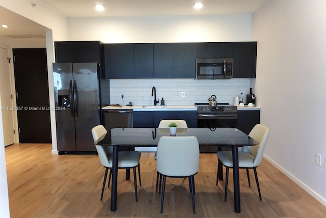 kitchen with sink, backsplash, light hardwood / wood-style floors, and black appliances