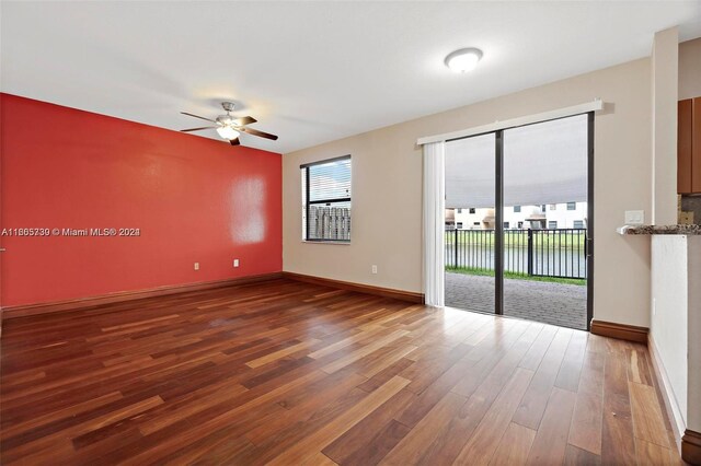 empty room with a water view, dark hardwood / wood-style floors, and ceiling fan