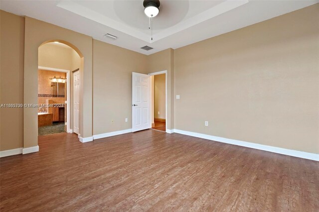 empty room with wood-type flooring, a tray ceiling, and ceiling fan