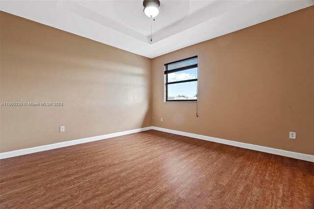 empty room featuring ceiling fan, hardwood / wood-style flooring, and a tray ceiling