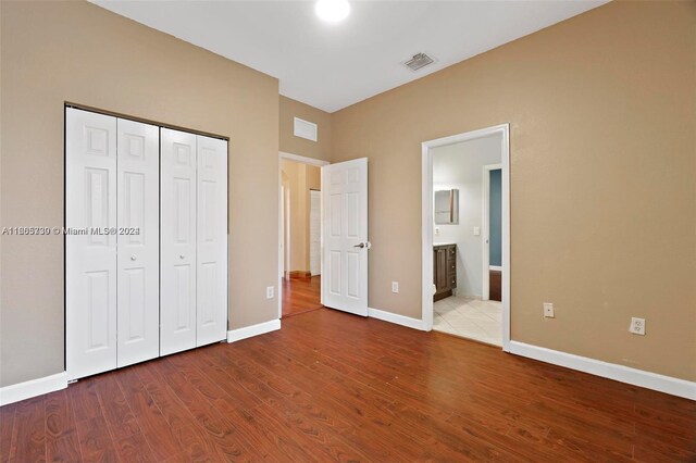 unfurnished bedroom with connected bathroom, hardwood / wood-style floors, and a closet