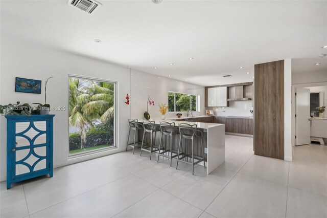 kitchen featuring wall chimney exhaust hood, a kitchen bar, kitchen peninsula, and plenty of natural light