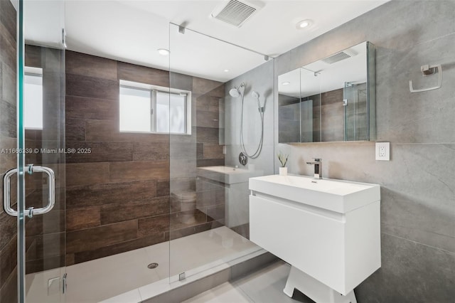 bathroom with vanity, a shower with door, and tile walls