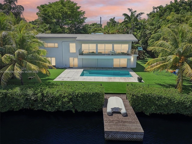 back house at dusk featuring a yard, a patio, a balcony, and a water view