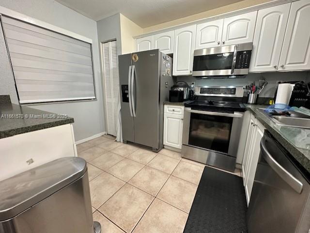 kitchen featuring appliances with stainless steel finishes, light tile patterned floors, and white cabinetry