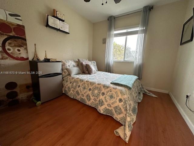 bedroom featuring stainless steel fridge, ceiling fan, and dark wood-type flooring