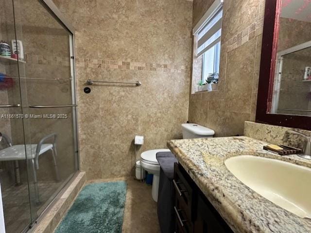 bathroom with vanity, toilet, tile walls, and a shower with shower door