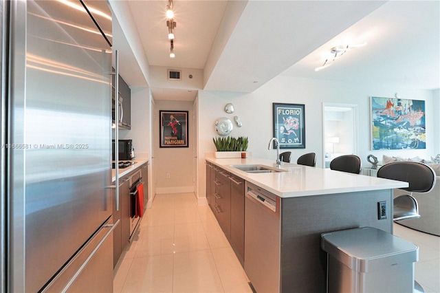 kitchen with sink, rail lighting, appliances with stainless steel finishes, light tile patterned flooring, and a large island with sink