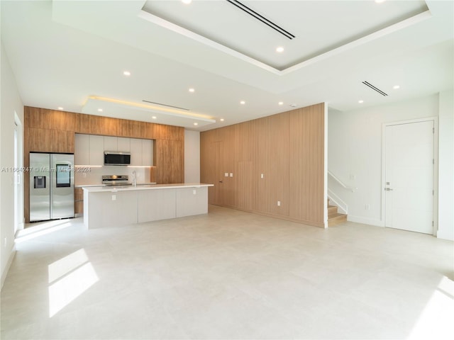 kitchen featuring wooden walls, a raised ceiling, appliances with stainless steel finishes, and a spacious island