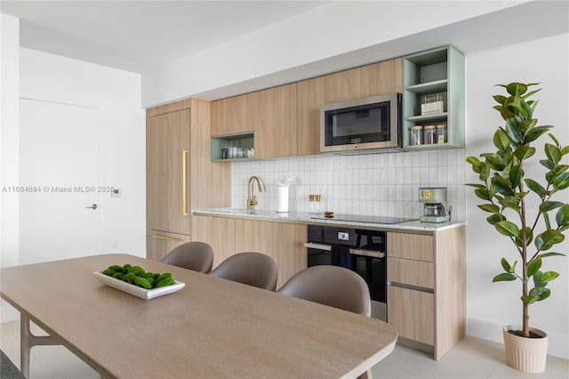 kitchen with light brown cabinetry, light stone countertops, decorative backsplash, and black appliances