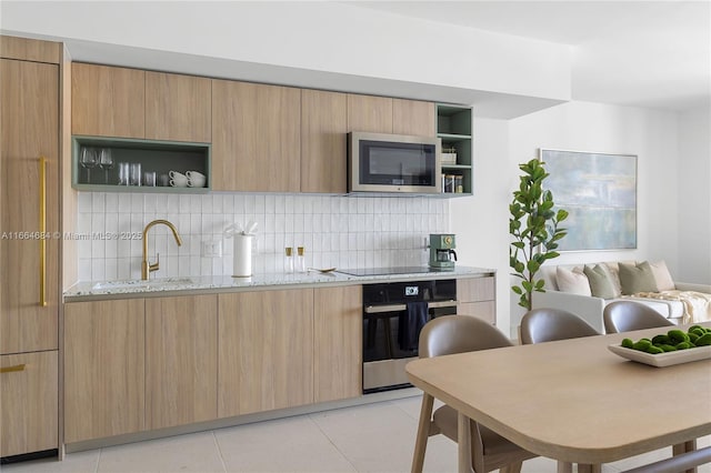 kitchen featuring light stone counters, stainless steel appliances, light brown cabinetry, and light tile patterned floors