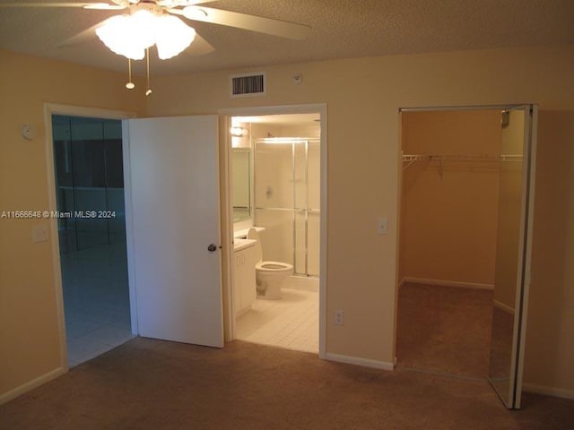 unfurnished bedroom with a closet, a textured ceiling, light colored carpet, ensuite bathroom, and ceiling fan