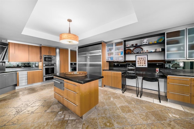 kitchen with built in appliances, a tray ceiling, a breakfast bar, and a kitchen island