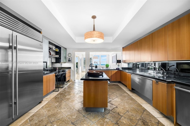 kitchen featuring appliances with stainless steel finishes, a kitchen island, a tray ceiling, decorative light fixtures, and sink