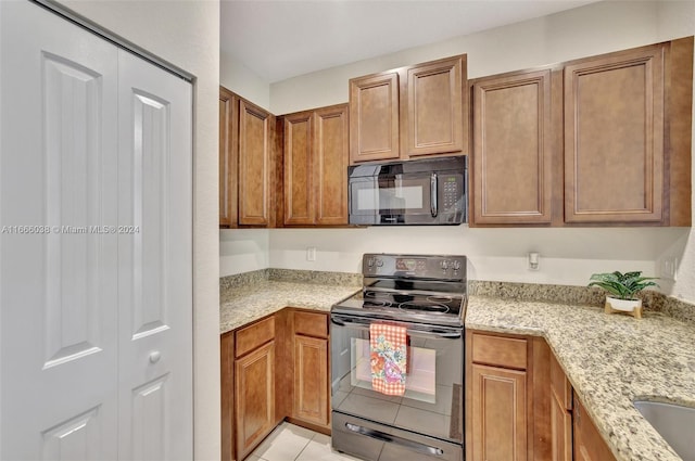 kitchen with black appliances, light tile patterned flooring, and light stone countertops