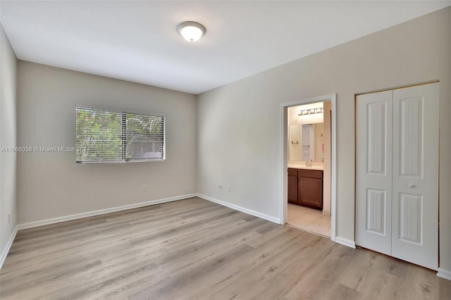 unfurnished bedroom with light hardwood / wood-style flooring, ensuite bath, and a closet