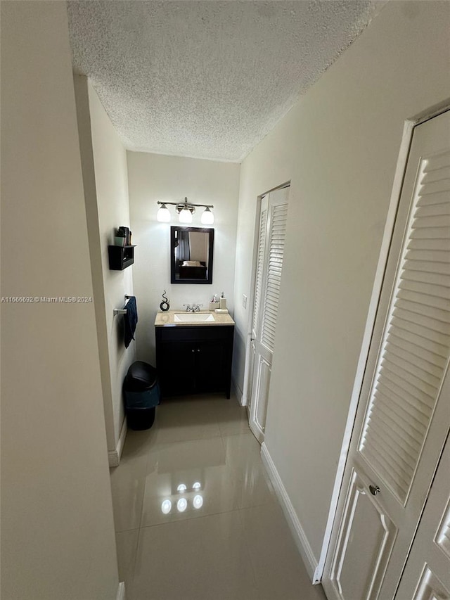 hallway featuring a textured ceiling, light tile patterned floors, and sink