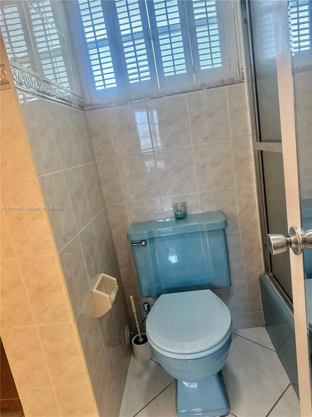 bathroom featuring tile walls, tile patterned floors, enclosed tub / shower combo, and toilet