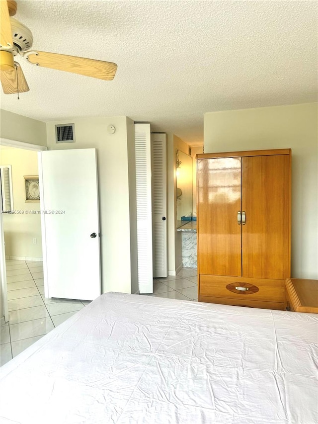 tiled bedroom with ceiling fan, a textured ceiling, and a closet