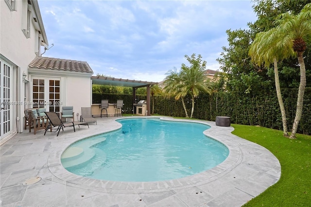 view of pool with french doors, a patio area, grilling area, and a lawn