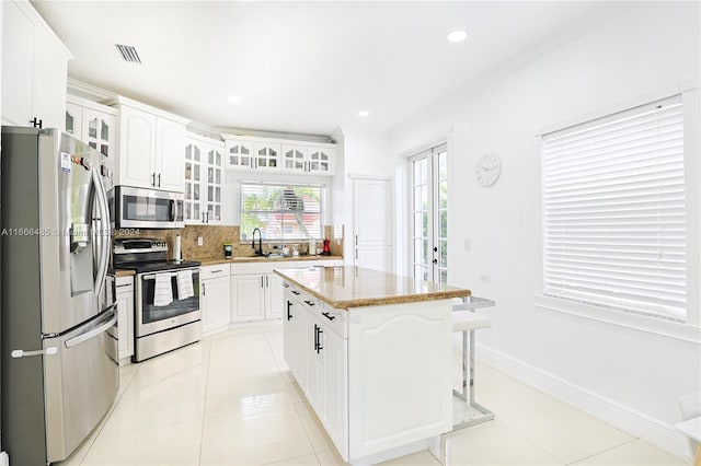 kitchen with appliances with stainless steel finishes, white cabinetry, light tile patterned flooring, tasteful backsplash, and a kitchen island