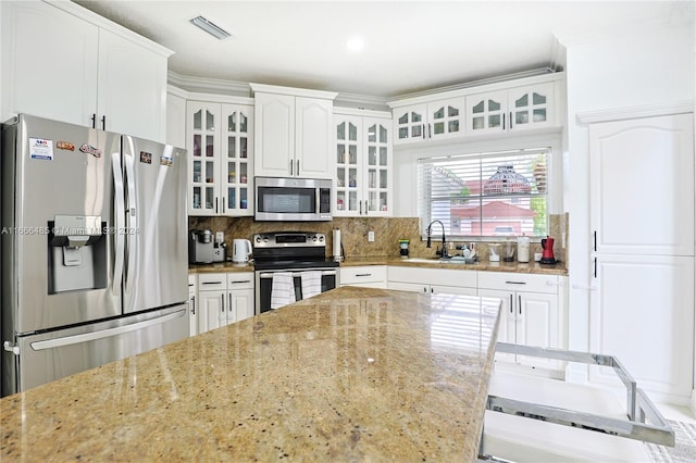 kitchen with sink, white cabinetry, backsplash, appliances with stainless steel finishes, and light stone countertops