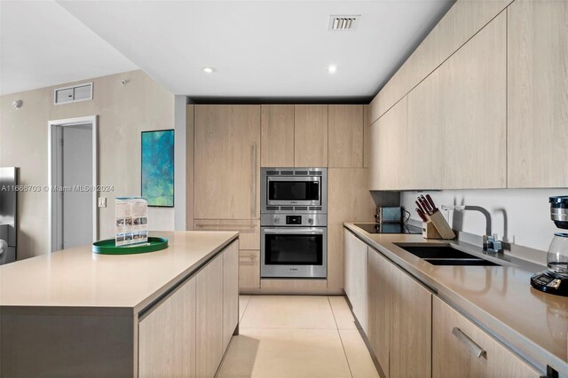 kitchen featuring appliances with stainless steel finishes, a kitchen island, light brown cabinets, light tile patterned floors, and sink