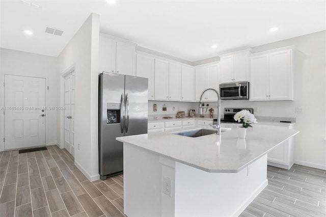 kitchen with white cabinetry, light wood-type flooring, appliances with stainless steel finishes, sink, and a kitchen island with sink