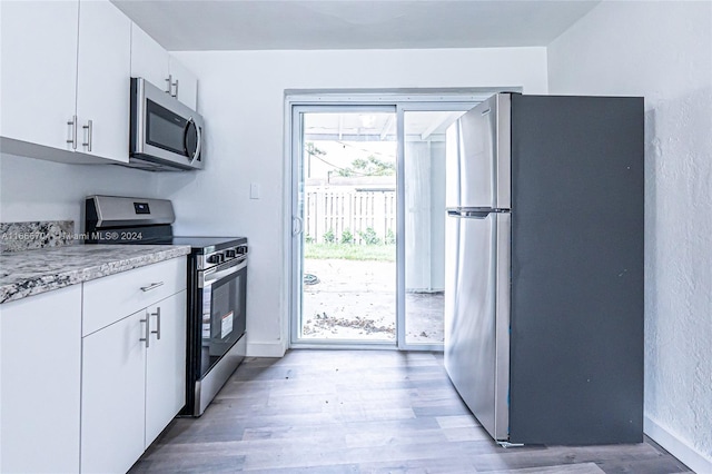 kitchen with white cabinets, light hardwood / wood-style floors, light stone countertops, and appliances with stainless steel finishes