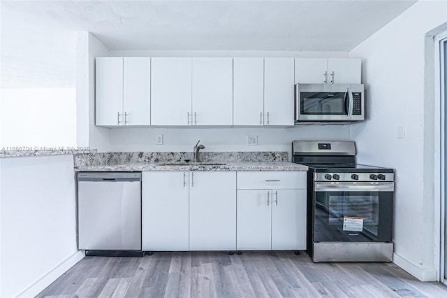 kitchen with light stone countertops, stainless steel appliances, light wood-type flooring, white cabinetry, and a sink