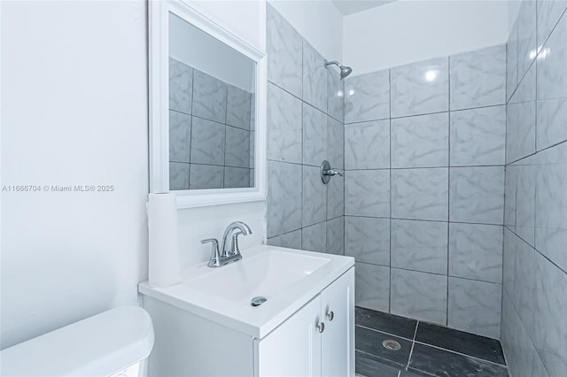 full bathroom with a tile shower, vanity, and toilet