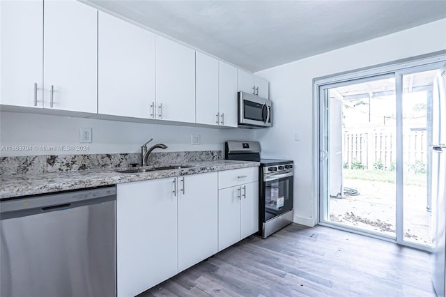 kitchen featuring white cabinets, sink, light stone countertops, light wood-type flooring, and stainless steel appliances