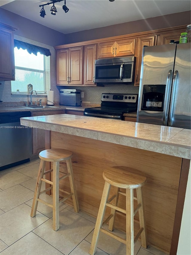 kitchen featuring light tile patterned flooring, appliances with stainless steel finishes, tasteful backsplash, and a kitchen breakfast bar