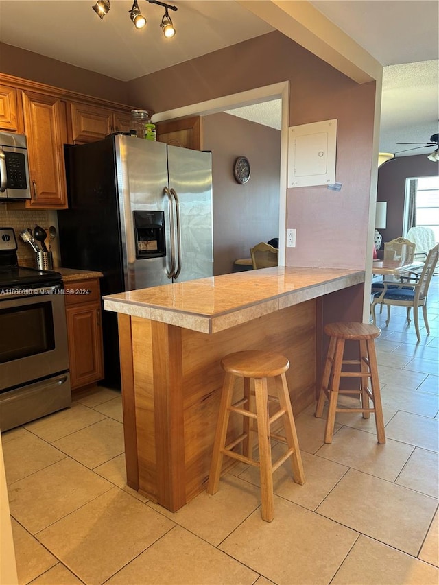 kitchen with ceiling fan, kitchen peninsula, backsplash, appliances with stainless steel finishes, and a breakfast bar area