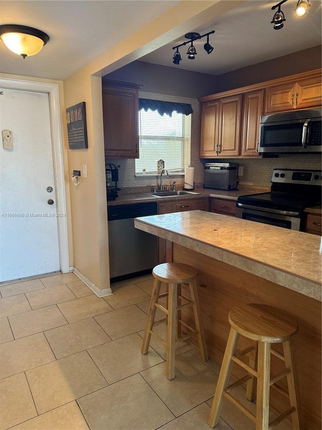 kitchen with sink, track lighting, stainless steel appliances, a kitchen bar, and decorative backsplash