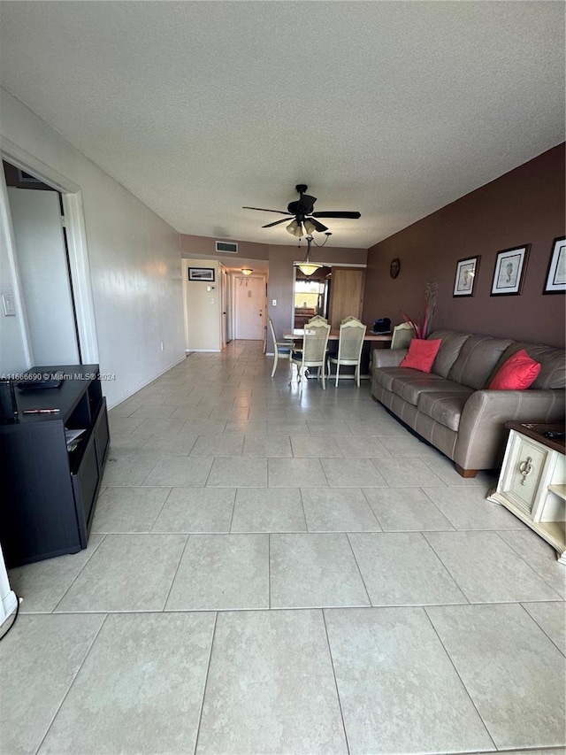 living room featuring a textured ceiling, light tile patterned floors, and ceiling fan