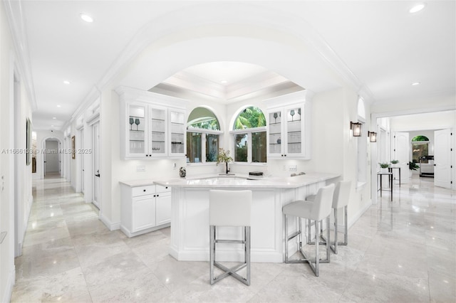 kitchen featuring a kitchen bar, a raised ceiling, white cabinetry, and kitchen peninsula